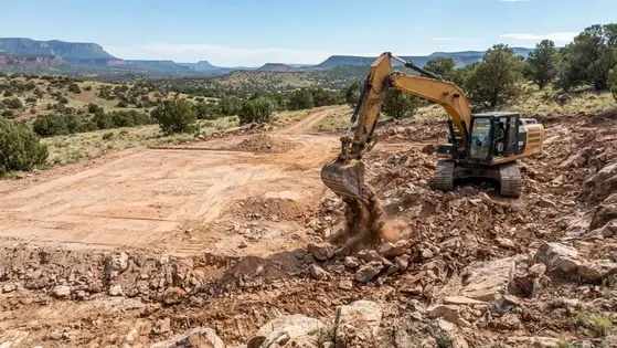 Excavator preparing rocky ground for a house pad on rural Apache County Arizona property
